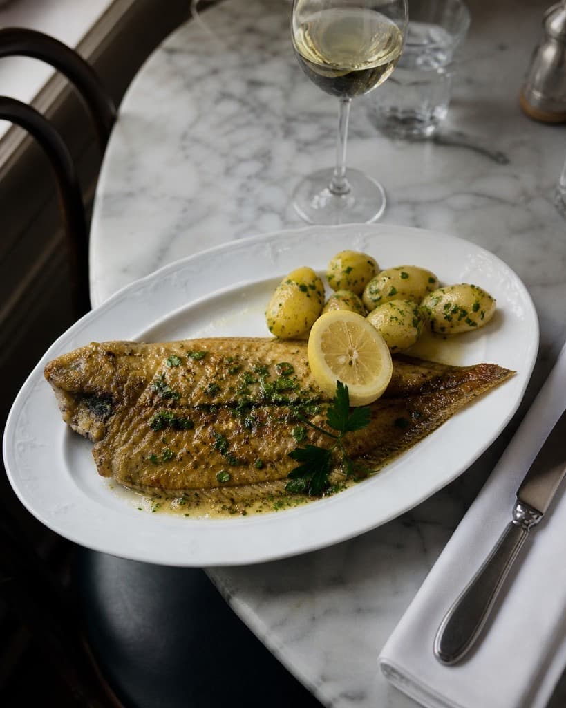 Sole meunière dorée au beurre, citron et persil sur assiette ovale blanche