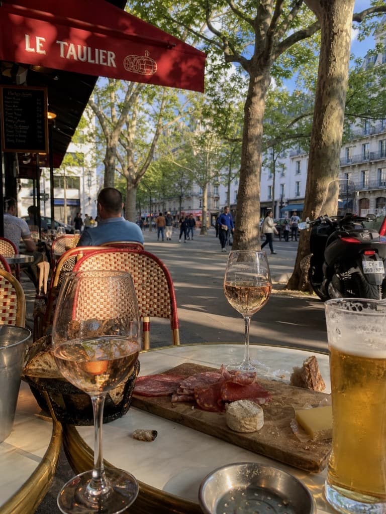 Terrasse côté avenue avec verres de rosé et planche apéro sous l’auvent rouge